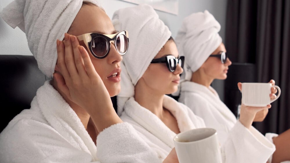 close up beautiful girls white bathrobes with towels head sunglasses drinking coffee bed hotel room.jpg